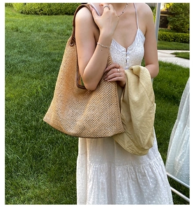 Detail of hand-woven straw tote with brown leather strap in natural outdoor setting