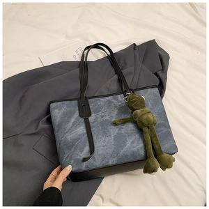 Detailed view of denim marble tote bag with black leather straps and green frog charm