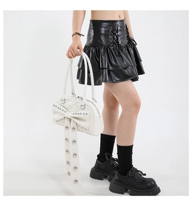 Close-up of a white tote bag with large studded bow, metallic rivets and long tassels