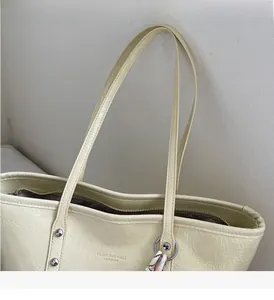 Dettaglio della borsa tote beige con trama in pelle plissettata e ciondolo in metallo
