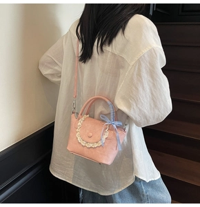Detail view of a pink crossbody bag with lace trim and blue checkered ribbon bow