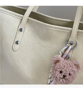 Dettaglio della borsa tote bianco crema con trama a pieghe e ciondolo a forma di orso