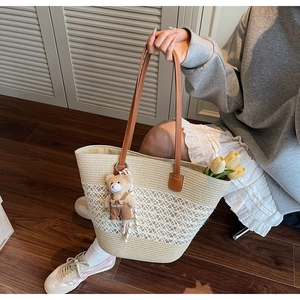 Detailed close-up of woven straw tote bag with lace overlay and cute plush bear charm