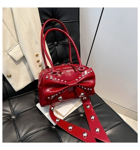 Detailed macro view of red patent leather handbag featuring silver studs and a large bow