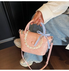 Detailed shot of pink glossy handbag with white lace trim and a blue checkered bow decoration