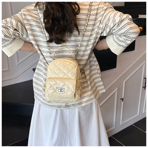 Detail eines beigen gesteppten Mini-Rucksacks mit silbernem Drehverschluss und Ketten