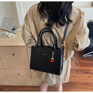 Detail der schwarzen Handtasche mit Kirsch-Anhänger auf einem modernen Schreibtisch