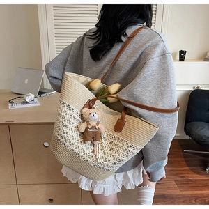 Detail of woven straw tote bag featuring contrast colors, leather strap and teddy charm