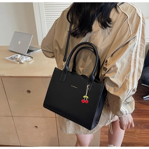 Elegante schwarze PU-Lederhandtasche mit Kirsch-Anhänger am Modell in Alltagsszene