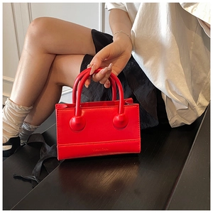 Detail of red leather handbag with unique sphere handle ornament and logo