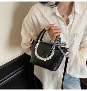 Detail showing glossy black leather texture with white lace trim and checkered bow accent