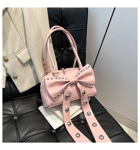 Detailed close-up of pink handbag with bow and silver studs on a stylish leather chair