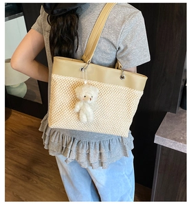 Close-up of woven straw tote bag with leather拼接 and cute white teddy bear charm accessory