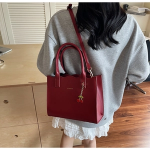 Detailansicht der tiefroten Brauthardtasche mit Goldlogo und Kirschanhänger-Zubehör