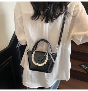 Close-up of black patent leather bag with pleated texture, lace trim and plaid ribbon handle