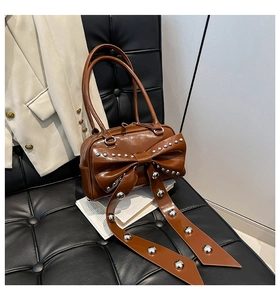 Detail of a brown patent leather handbag featuring a large studded bow on a leather sofa
