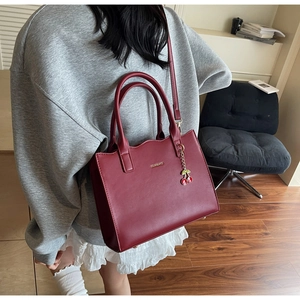 Detail der weinroten Leder-Tote-Bag mit Kirsch-Anhänger an einem Model zu Hause