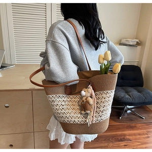 Detail of woven straw tote bag with brown leather handles and plush bear charm