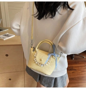 Detail of yellow pleated leather crossbody bag with white lace trim and plaid bow handle