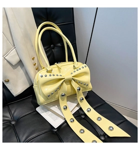 Detail of pale yellow glossy handbag featuring large bow and metallic rivet studs