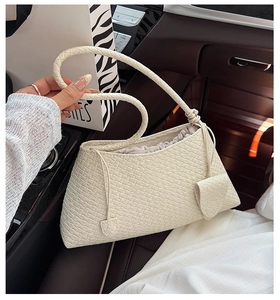 Close-up of beige woven texture shoulder bag with drawstring closure in a car interior setting