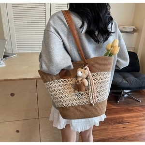 Detail view of woven straw tote bag with white hollow-out mesh and brown leather straps