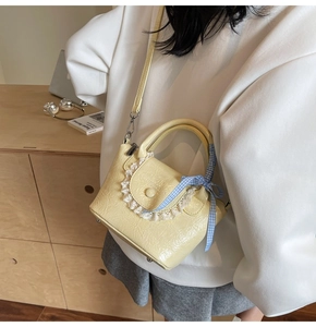 Detail view of yellow crossbody bag with white lace trim and blue checkered ribbon bow