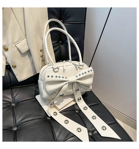 Close-up of cream handbag featuring a large bow and silver studs on black leather bench
