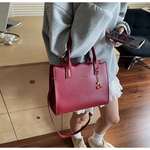 Details der burgunderfarbenen Brauthndtasche mit Goldlogo und Kirsch-Anhänger