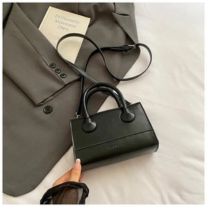 Detail of black leather crossbody bag featuring embossed logo on grey suit fabric