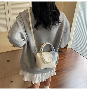 Close-up of cream leather handbag with lace trim and blue checkered bow detail
