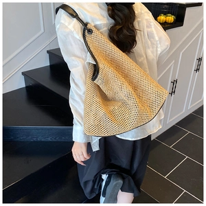 Detail showing the large woven straw tote with black leather straps on a model's shoulder