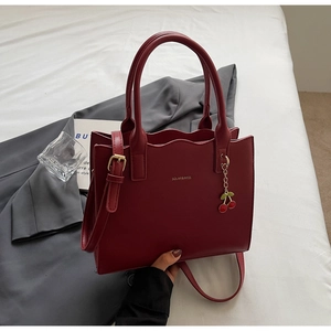 Nahaufnahme der eleganten weinroten Handtasche mit Wellenkante und Kirsch-Anhänger Detail