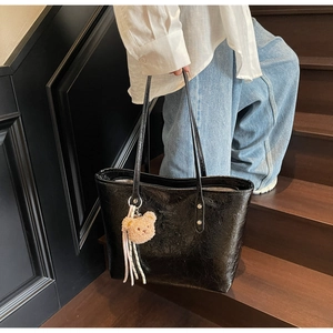 Dettaglio della borsa tote nera con texture in pelle stropicciata e ciondolo a orsetto
