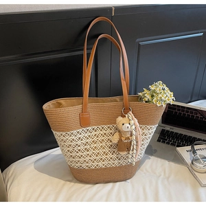 Detail of woven straw tote bag with brown leather handles and a cute bear pendant on a bed