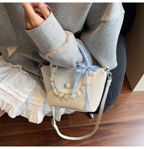 Detail of cream lace handbag with blue checkered bow worn by a model in casual outfit