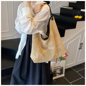 Detail of large woven straw tote bag featuring black shoulder strap and hollow pattern