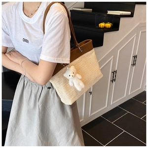 Detail of woven straw tote bag with brown leather trim and cute white plush bear charm