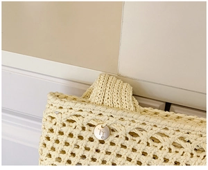 Detail of hollow woven handbag featuring a silver metal logo tag with a small diamond