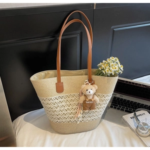 Detail of woven straw tote bag with brown leather straps and cute bear pendant