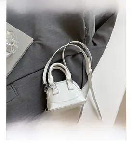 Détail d'un sac coquillage en cuir verni blanc avec surpiqûres sur fond de veste grise