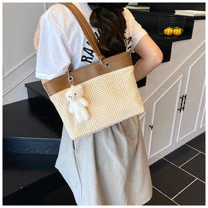 Detail of cream straw tote bag with brown leather straps and cute bear charm pendant