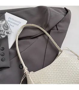 Detail of beige hand-woven leather bag with woven shoulder strap on a grey suit