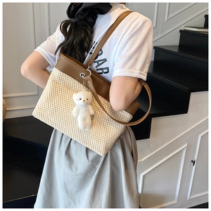 Detail of woven straw tote bag with brown leather trim and cute white plush bear charm