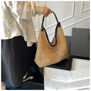 Detailed close-up of woven beige straw tote bag featuring black leather trim and metal rings