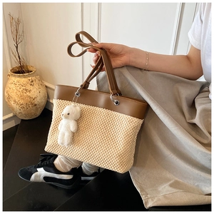 Close-up of woven straw tote bag with brown leather handles and a cute bear charm