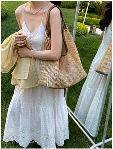 Close-up of woven straw tote bag with leather straps on a model in nature