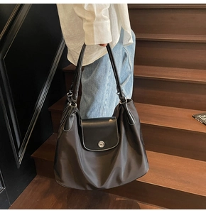 Detail of black nylon tote bag with leather flap featuring contrast white stitching