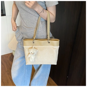 Detail view of woven straw tote bag featuring leather patchwork and a white teddy bear charm