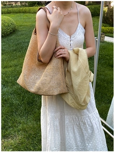 Detail of woven straw tote bag with brown leather handles on a natural green grass background